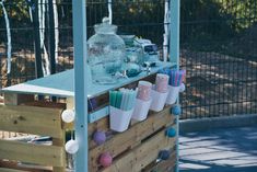 a wooden cart with cups and other items on it in front of a fenced area