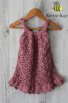 a pink crocheted dress hanging on a wooden hanger with a bee in the background