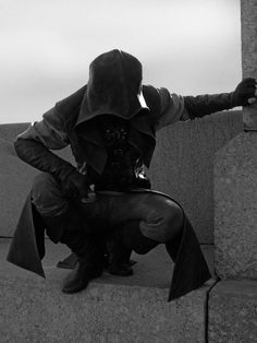 a man dressed in black sitting on top of a stone wall with his arms outstretched