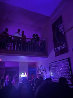 a group of people standing on top of a balcony next to a purple lit room