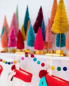 brightly colored christmas trees are hanging on the mantles in front of a white wall