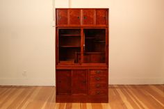 a wooden bookcase with drawers on top of it in an empty room next to a wall