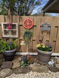 three pots with plants in them next to a wooden fence and some rocks on the ground