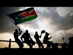 silhouettes of people running with a flag in front of a fence and cloudy sky