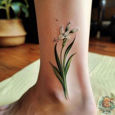 a small flower tattoo on the ankle with green leaves and white flowers in it's center