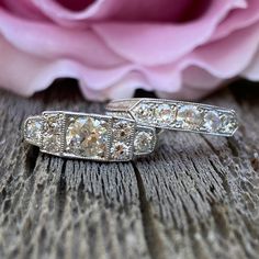 two wedding rings sitting on top of a wooden table next to a pink rose with petals