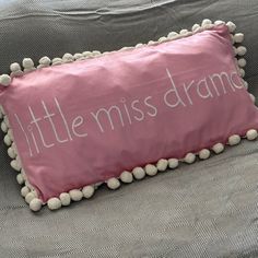 a pink pillow with white pom - poms that says little miss drama on it