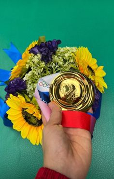 a person holding a gold medal in front of sunflowers and other colorful flowers