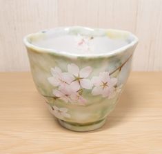 a white and pink flowered bowl sitting on top of a wooden table next to a wall