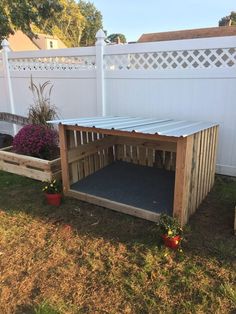 a dog house made out of wooden pallets in the yard with plants and flowers around it