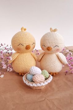 two small crocheted chickens sitting next to each other in a basket filled with eggs