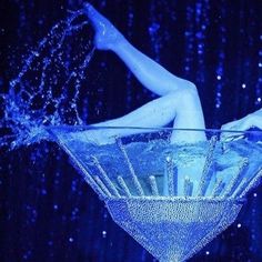 a woman is floating in the water on top of a martini glass with blue lights