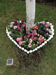 a heart shaped planter with mushrooms and flowers in the grass next to a tree