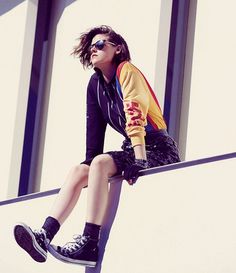 a woman sitting on top of a metal rail with her legs crossed and wearing black sneakers