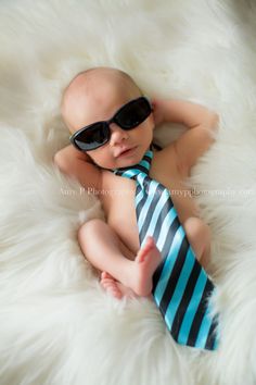 a baby wearing sunglasses and a tie laying on top of a fluffy white blanket with his hands behind his head