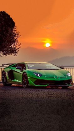 a green sports car parked in front of a fence with the sun setting behind it