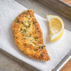 a piece of breaded chicken on a napkin next to a lemon wedge