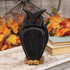 an owl figurine sitting on top of a table next to books and autumn leaves