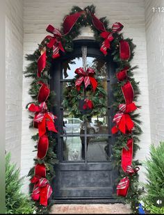 a christmas wreath on the front door of a house decorated with red and green bows