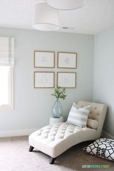 a white couch sitting in front of a window next to a wall with pictures on it