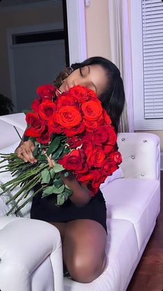 a woman sitting on a couch holding a bunch of red roses