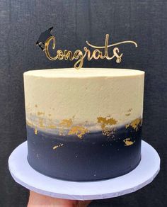 a blue and white cake with gold lettering that says congrats on top, in front of a black background