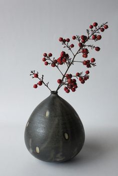 a gray vase with red berries in it