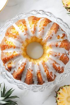 a pineapple bundt cake with white icing on a glass platter next to sliced pineapples