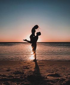 a woman standing on top of a sandy beach next to the ocean at sun set