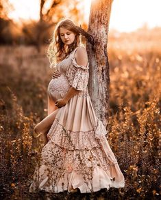 a pregnant woman leaning against a tree in a field