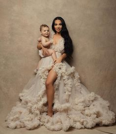 a woman in a dress holding a baby while posing for a photo with her legs spread out