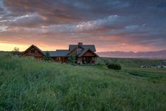 a large house sitting on top of a lush green hillside under a cloudy sky with mountains in the background