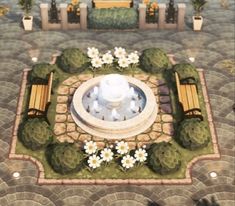 an aerial view of a fountain surrounded by flowers and benches