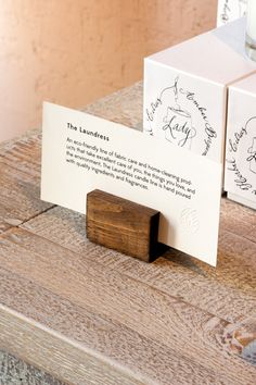 two business cards are sitting on a wooden table next to a candle and some boxes