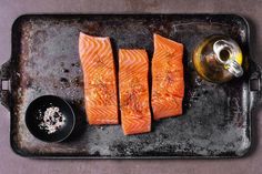 four salmon fillets on a baking pan with seasoning and salt next to them