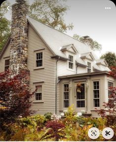 an old house is surrounded by trees and bushes with fall foliage on the front lawn