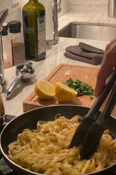 a person is cooking pasta in a pan with lemons and parsley on the side