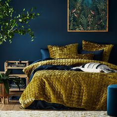 a bedroom with dark blue walls and gold bedding, potted plant in the corner