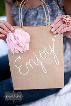 a woman holding a brown bag with the word enjoy written on it and a pink flower