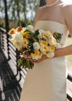 a woman in a white dress holding a bouquet of yellow and white flowers on her wedding day