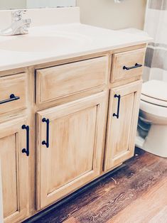 a white toilet sitting next to a wooden cabinet in a bathroom on top of a hard wood floor