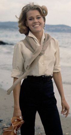 a woman standing on top of a beach next to the ocean holding a baseball glove