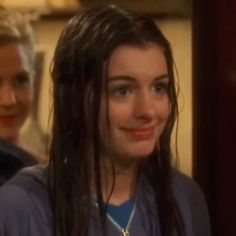 two women standing next to each other with long hair and blue shirts on, one is smiling at the camera