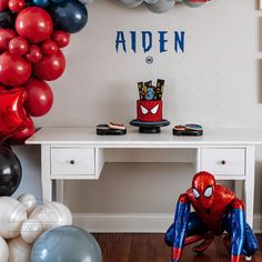 a spiderman themed birthday party with balloons and decorations on the wall, along with an office desk