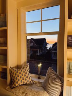 a window seat with pillows and a candle in front of it, next to some bookshelves