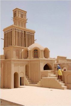 a man standing in front of a building made out of sand with stairs leading up to it