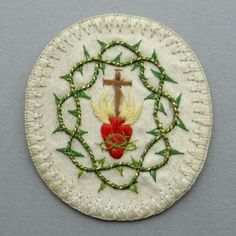 an embroidered cross and flower on a white plate with green leaves around it, sitting on a gray surface