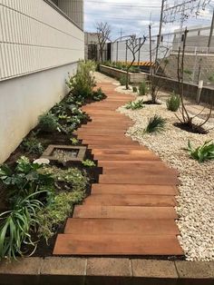 a wooden walkway in the middle of a yard with gravel and plants on both sides