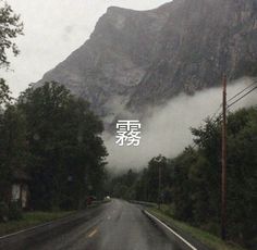 an image of a mountain with clouds in the sky and trees on the side of the road