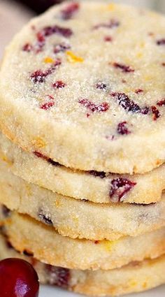 a stack of cookies sitting on top of a white plate next to two cherries